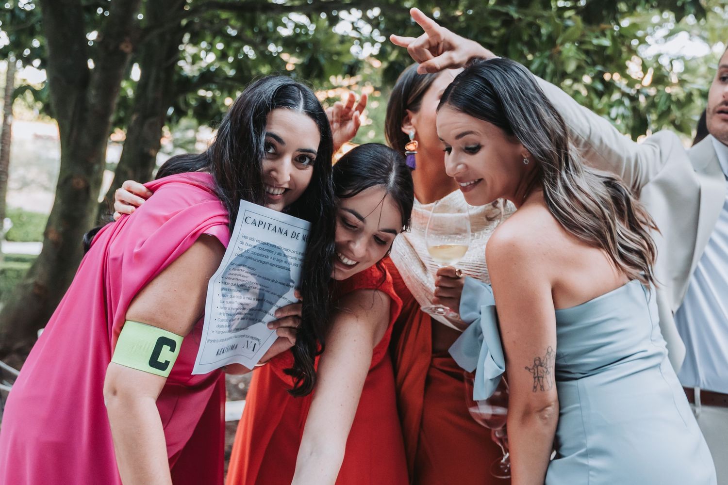 Wedding party members in pink and red dresses celebrate together outdoors.