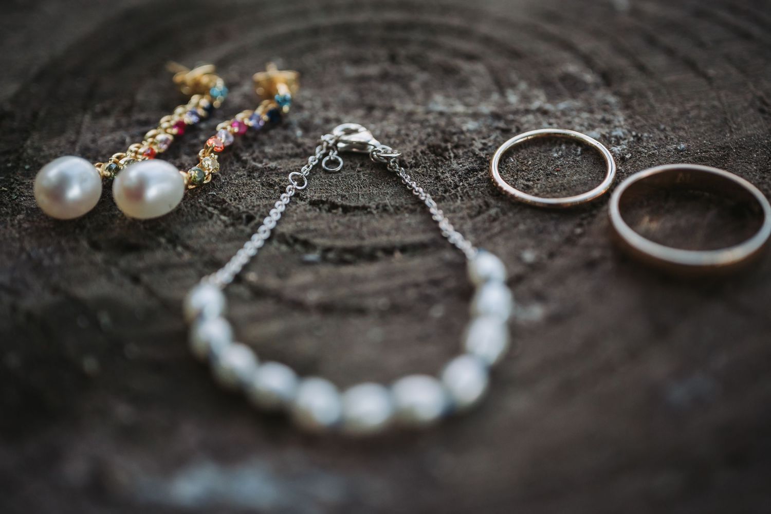 Wedding jewelry and accessories including pearl necklace, rings, and bracelets arranged on textured surface.