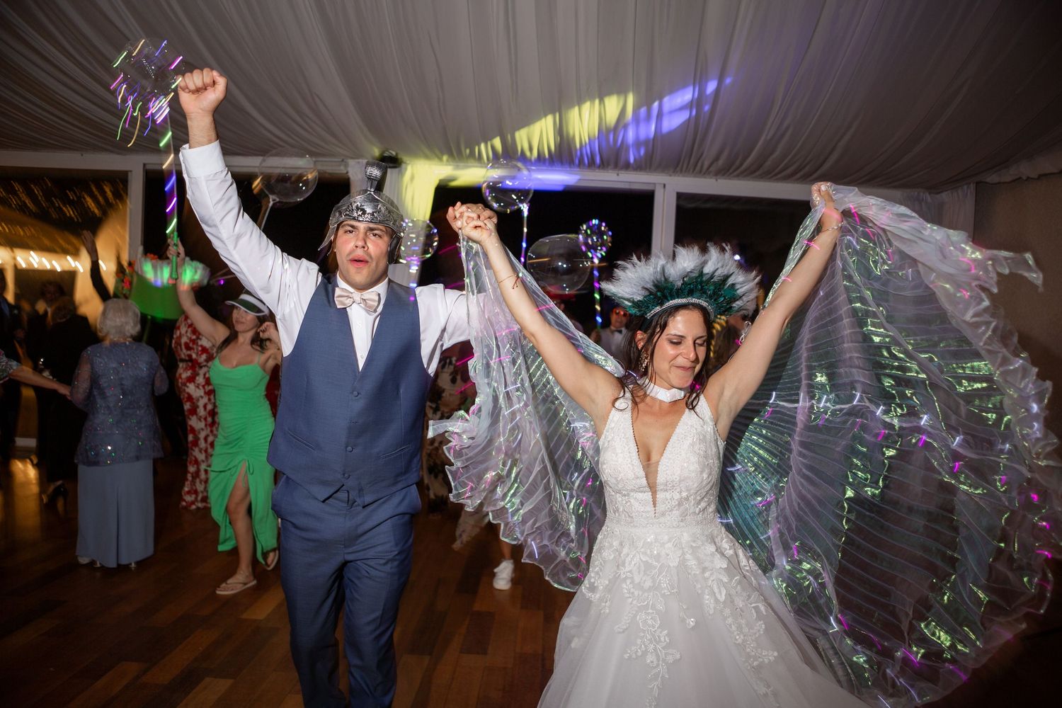 A couple celebrates with raised arms while dancing at their wedding reception under string lights.