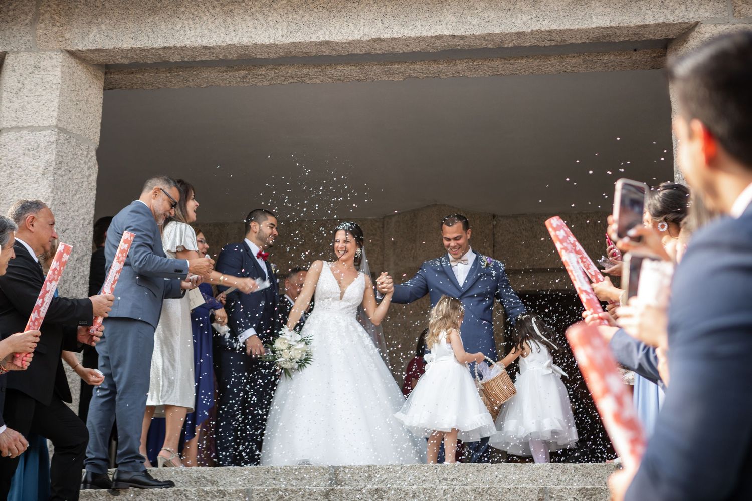 Joyful celebration outside a stone church as guests shower the couple with white confetti.