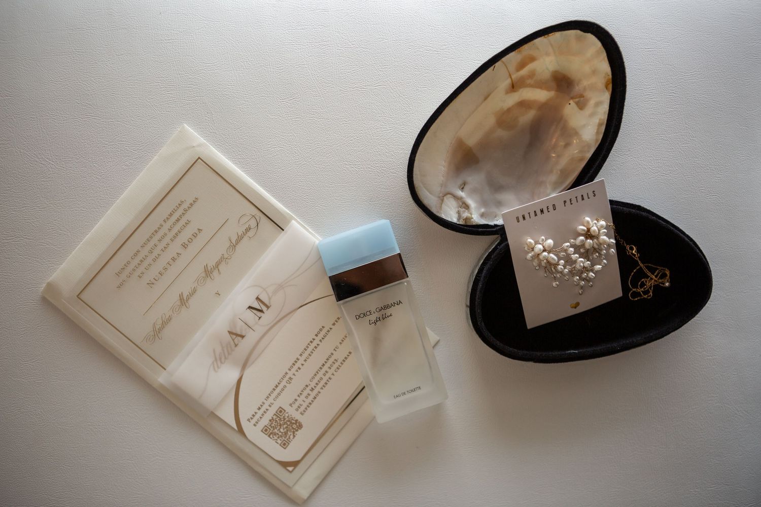 Wedding dress and accessories laid out on white background with invitation and jewelry.