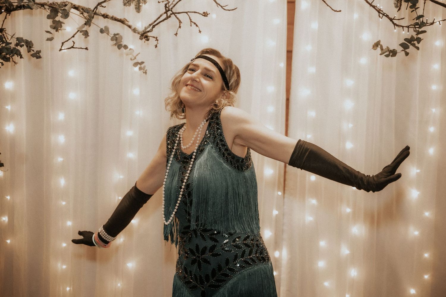 A dancer in a green top performs expressive movements against a backdrop of twinkling string lights.