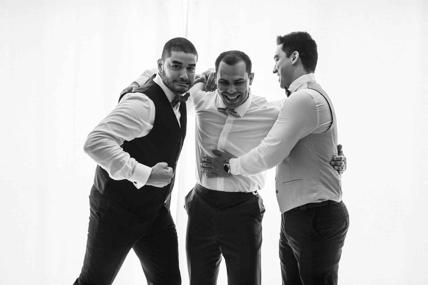 A group of people in formal attire lean forward and laugh together in a black and white photograph.