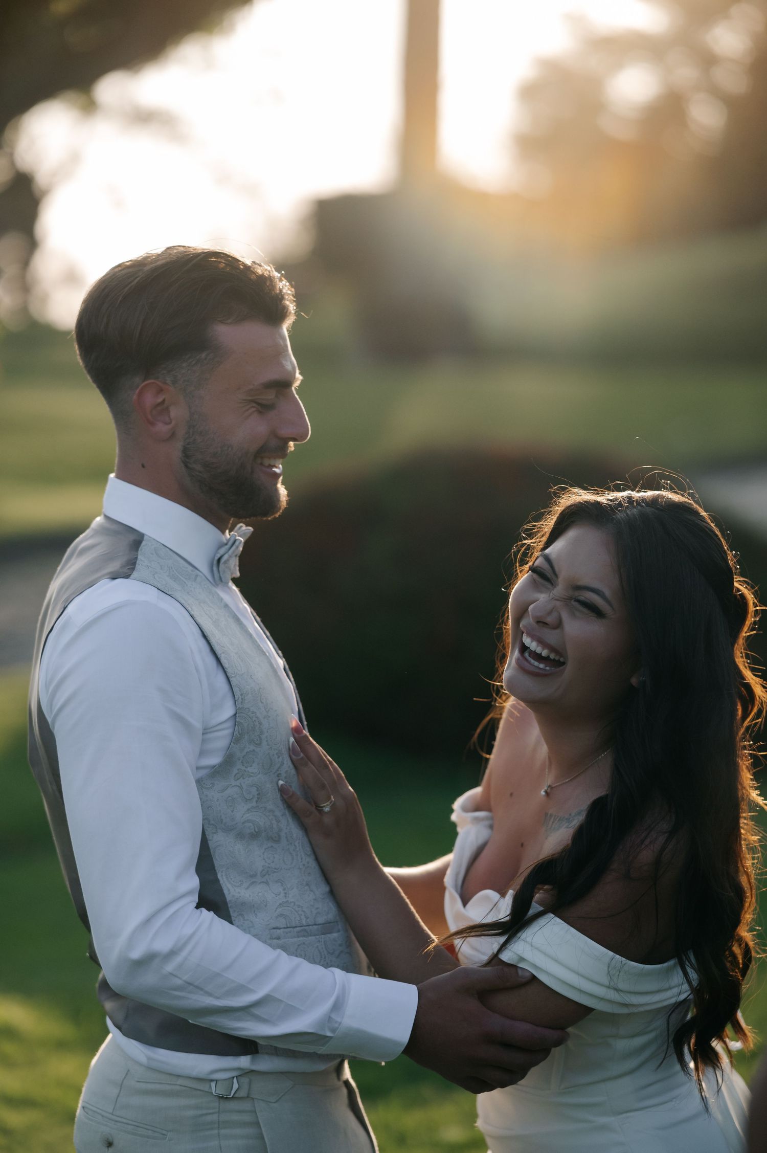 A couple shares joyful laughter together during a sunset photoshoot in a grassy field.