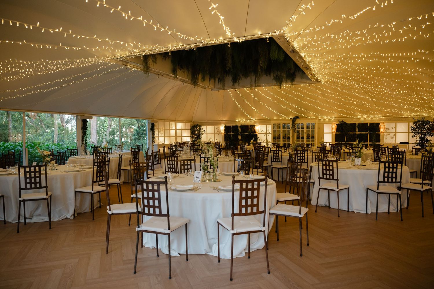 String lights create a magical canopy over elegant table settings in a white tent wedding reception space.