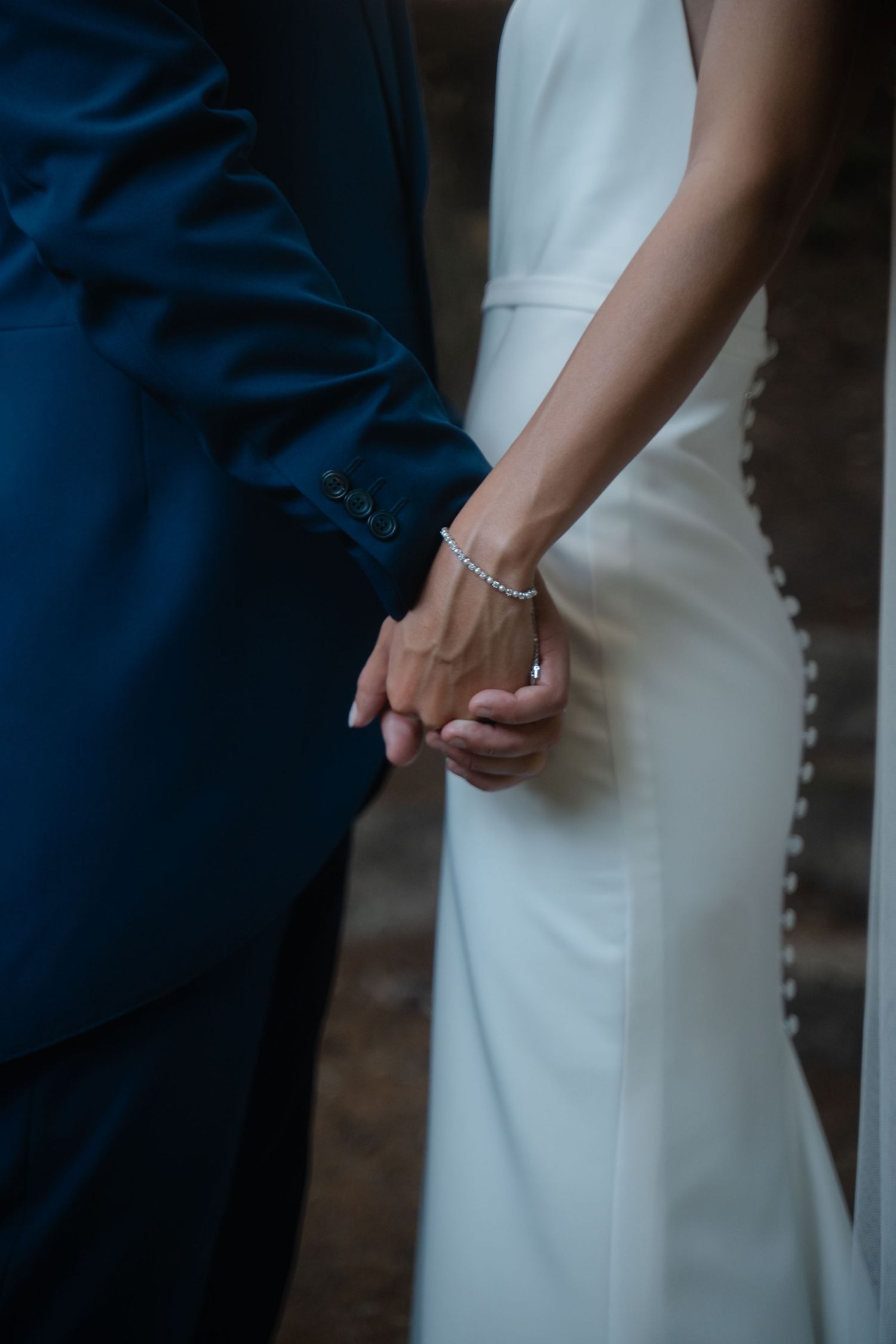 Close-up view of a couple holding hands, with one person wearing a navy suit and the other in a white dress.