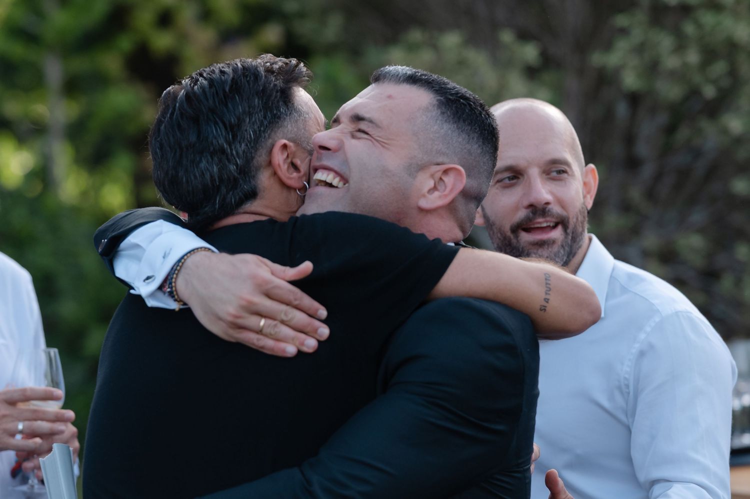 Two people share an emotional embrace while others look on during what appears to be an outdoor celebration.
