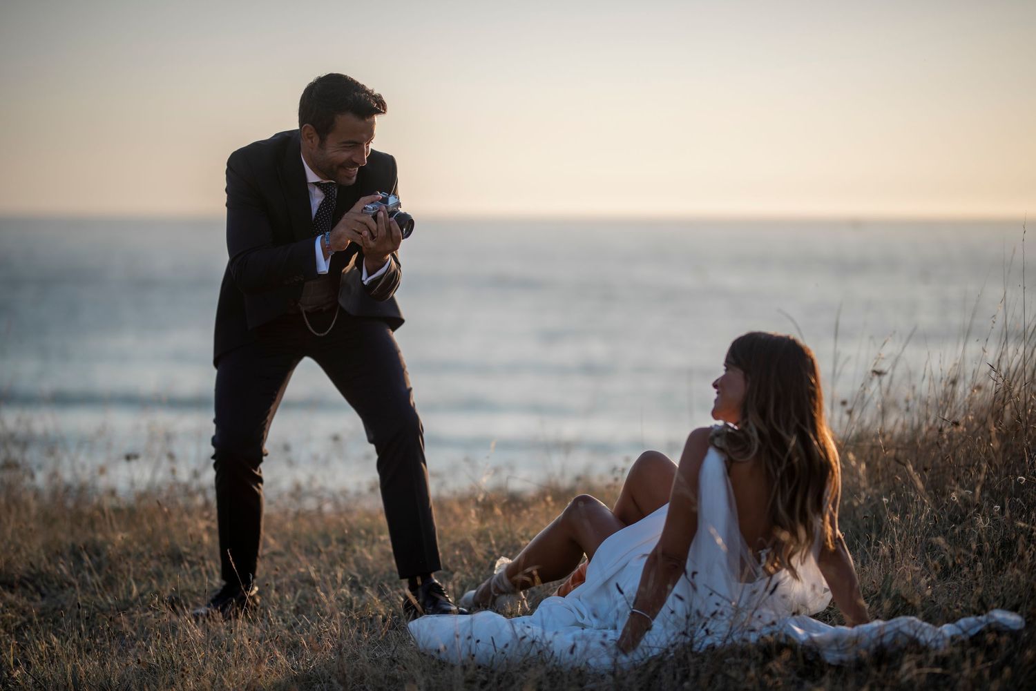 A couple embraces on a scenic beach during golden hour with waves crashing behind them.