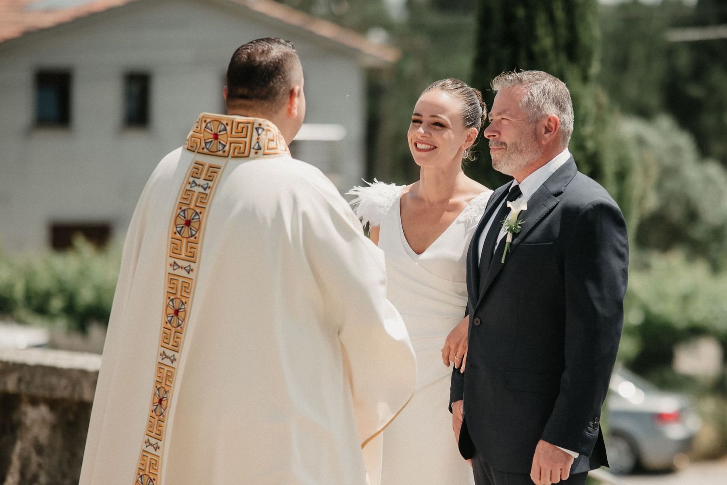 A couple shares a joyful moment during their wedding ceremony with an officiant in outdoor garden setting.