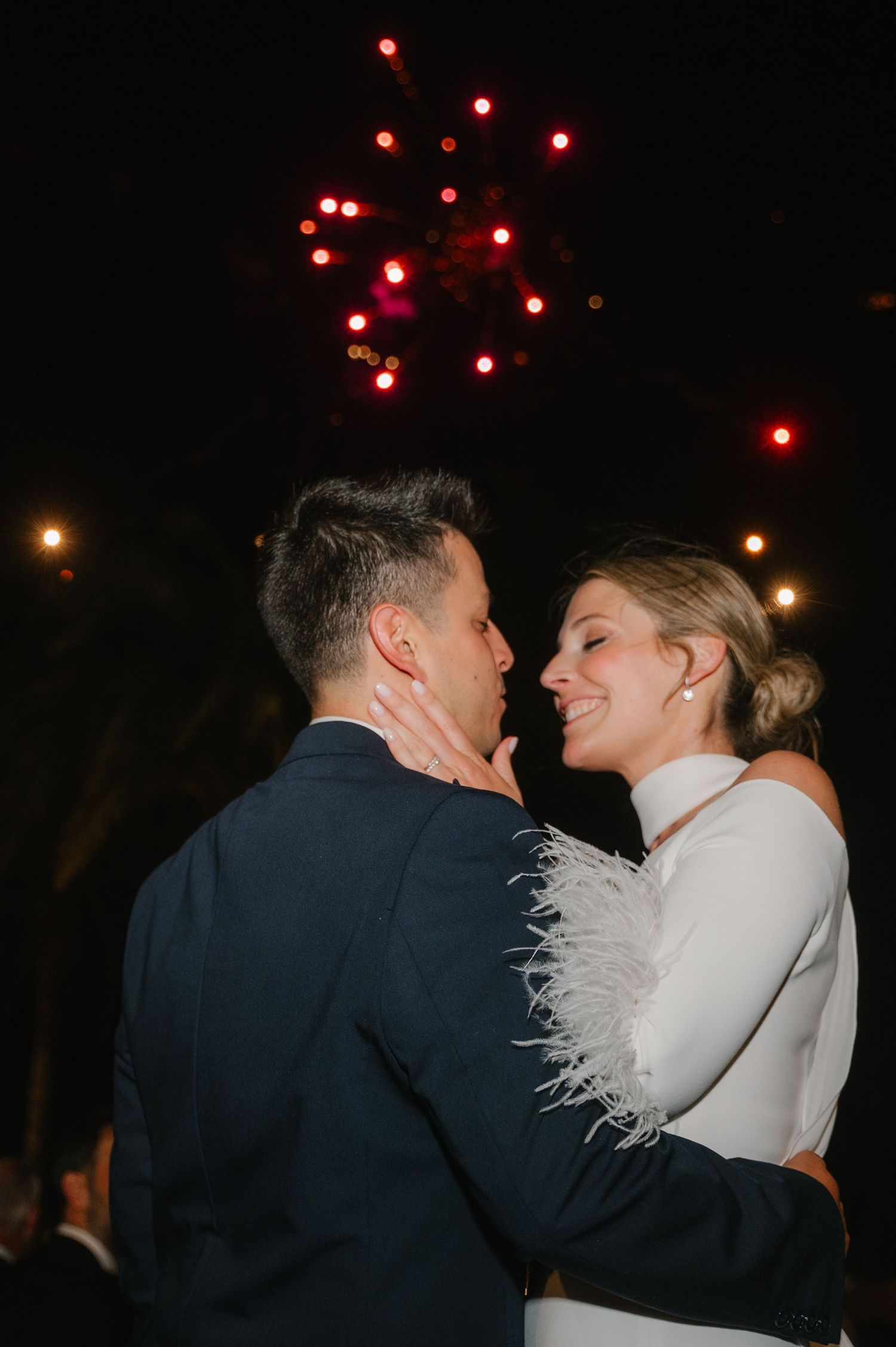 A romantic moment captured at a nighttime wedding celebration with glowing red lights in the background.