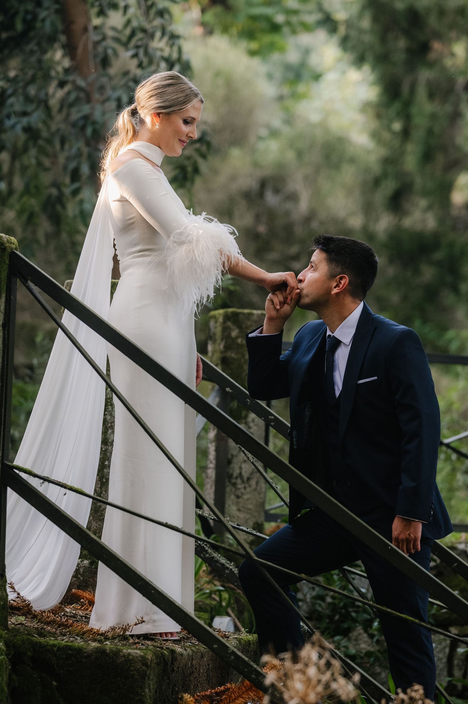 A couple in wedding attire shares an intimate moment on outdoor wooden stairs surrounded by greenery.