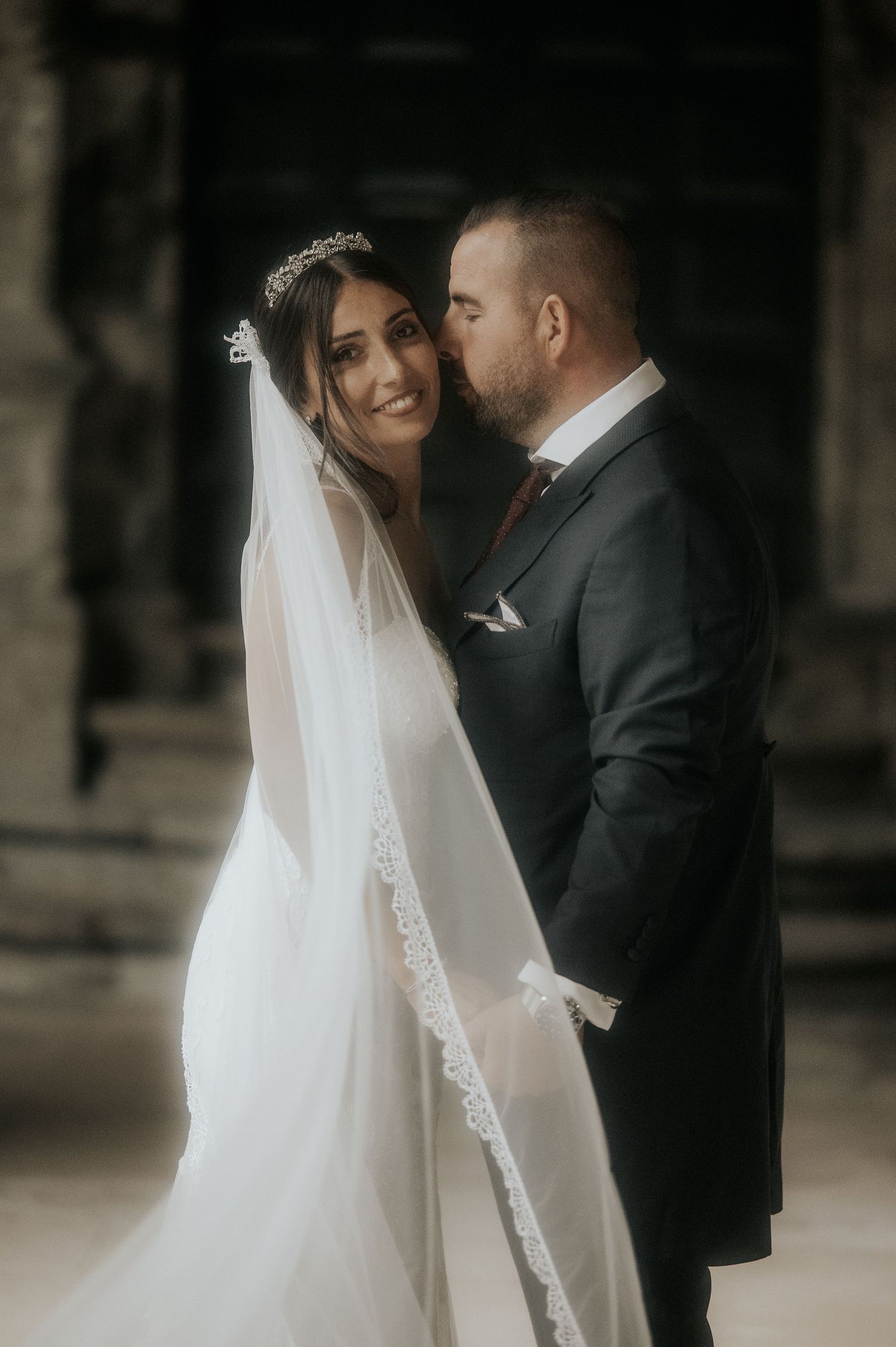 An intimate wedding portrait showing a tender moment between newlyweds in a moody, classic setting.