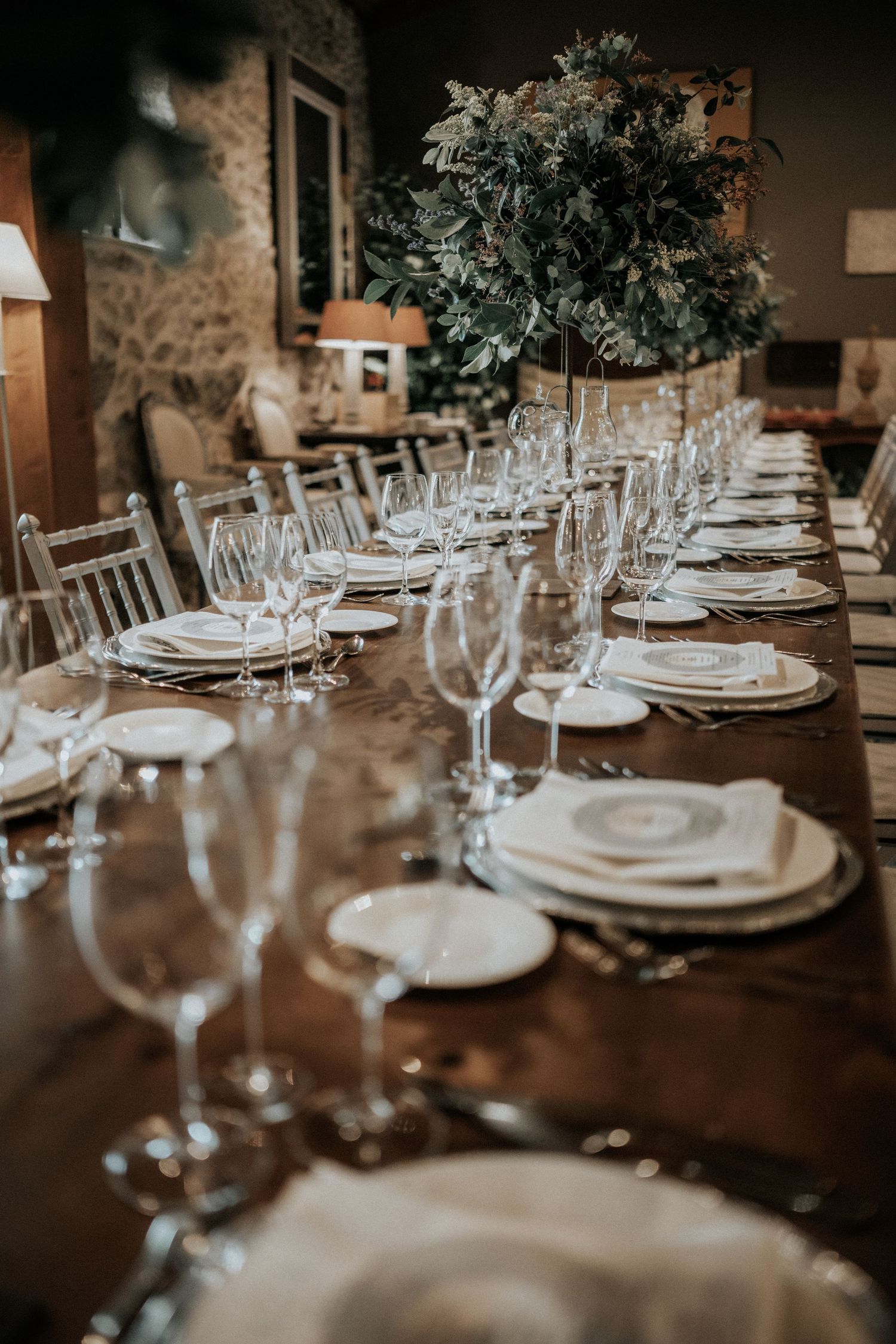 Elegant wedding reception table settings with white plates, wine glasses, and floral centerpieces on dark wooden tables.