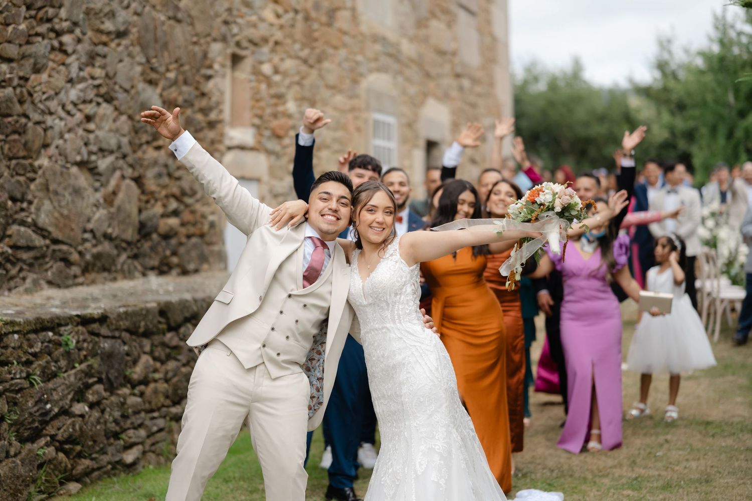 Wedding guests gather in front of a rustic stone wall during an outdoor celebration.