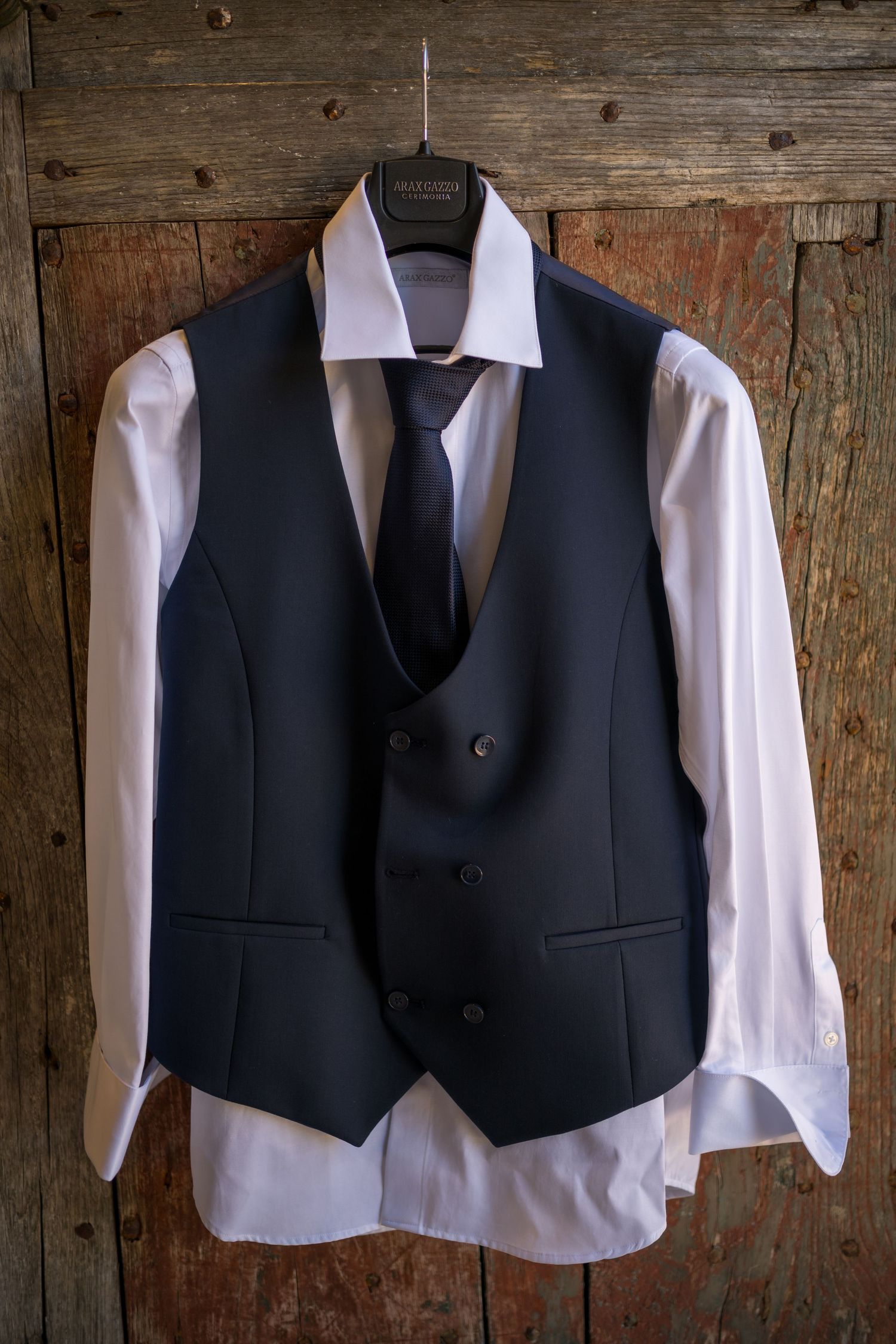 Three navy blue formal vests with white dress shirts hanging on wooden wall display.