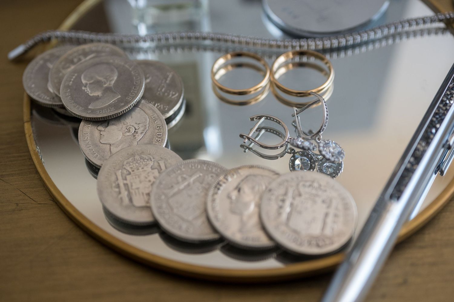 Silver coins and gold rings displayed on a reflective surface with a pen in the background.