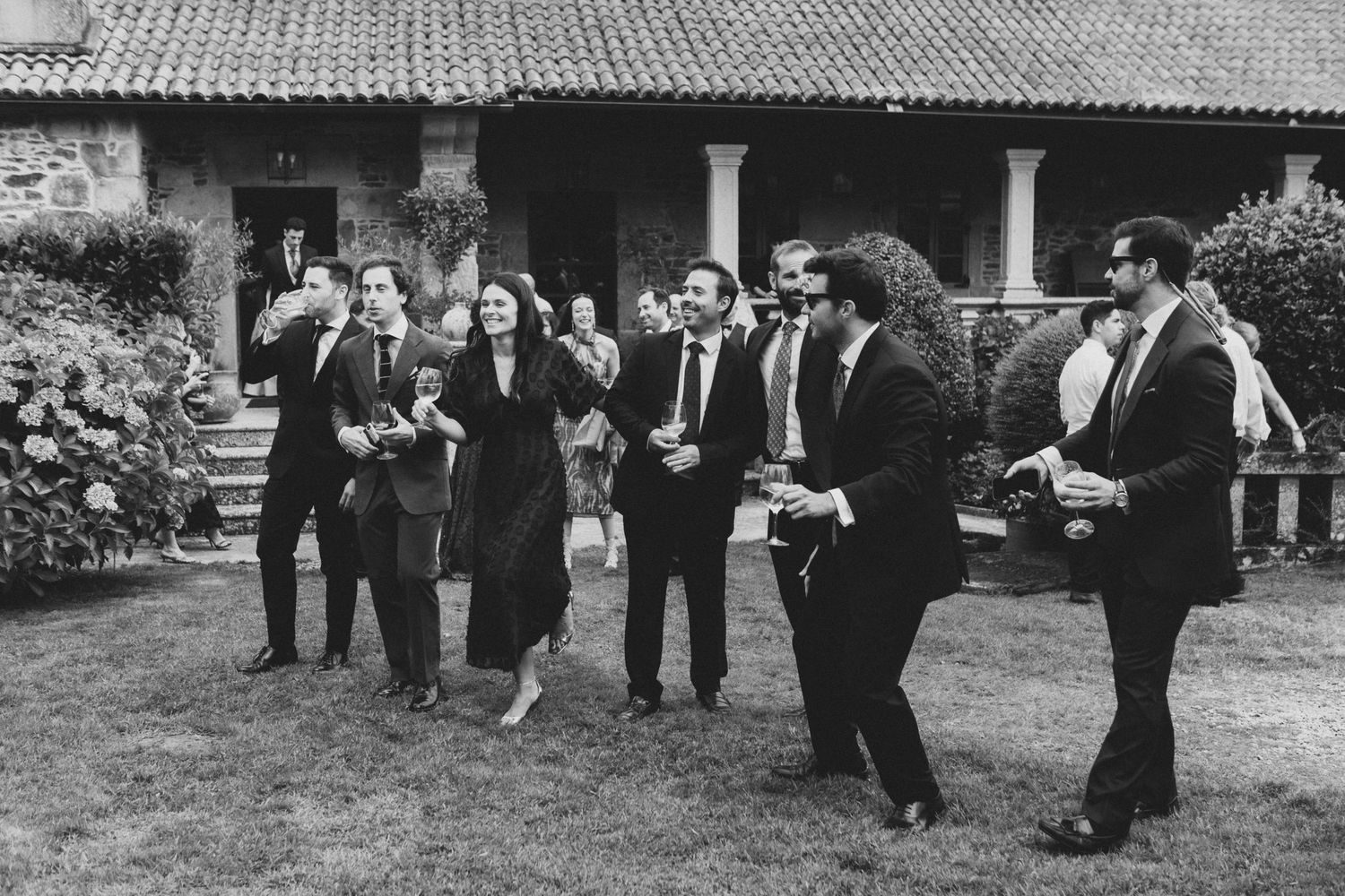 A vintage black and white photograph shows a group of people dancing together in a line outdoors.