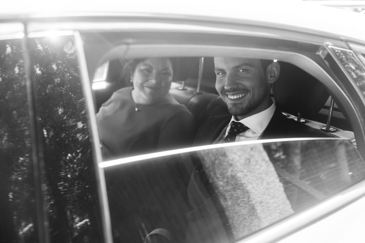 A black and white photograph showing passengers smiling through a car window.