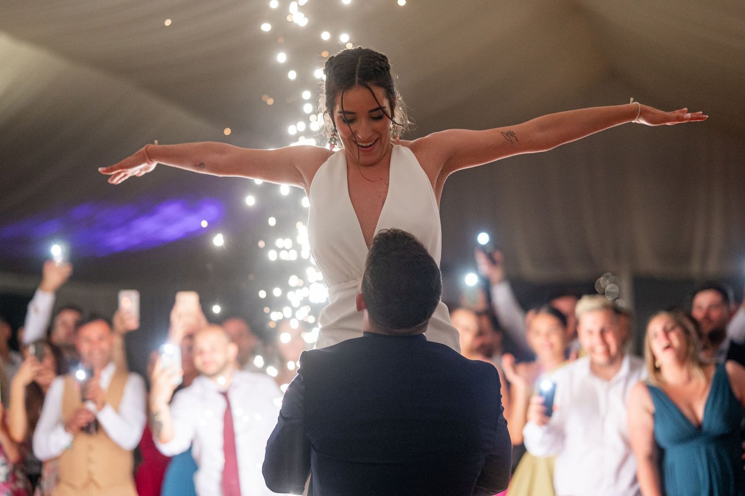 A joyous celebration on a wedding dance floor with sparkling lights and guests watching the couple's first dance.