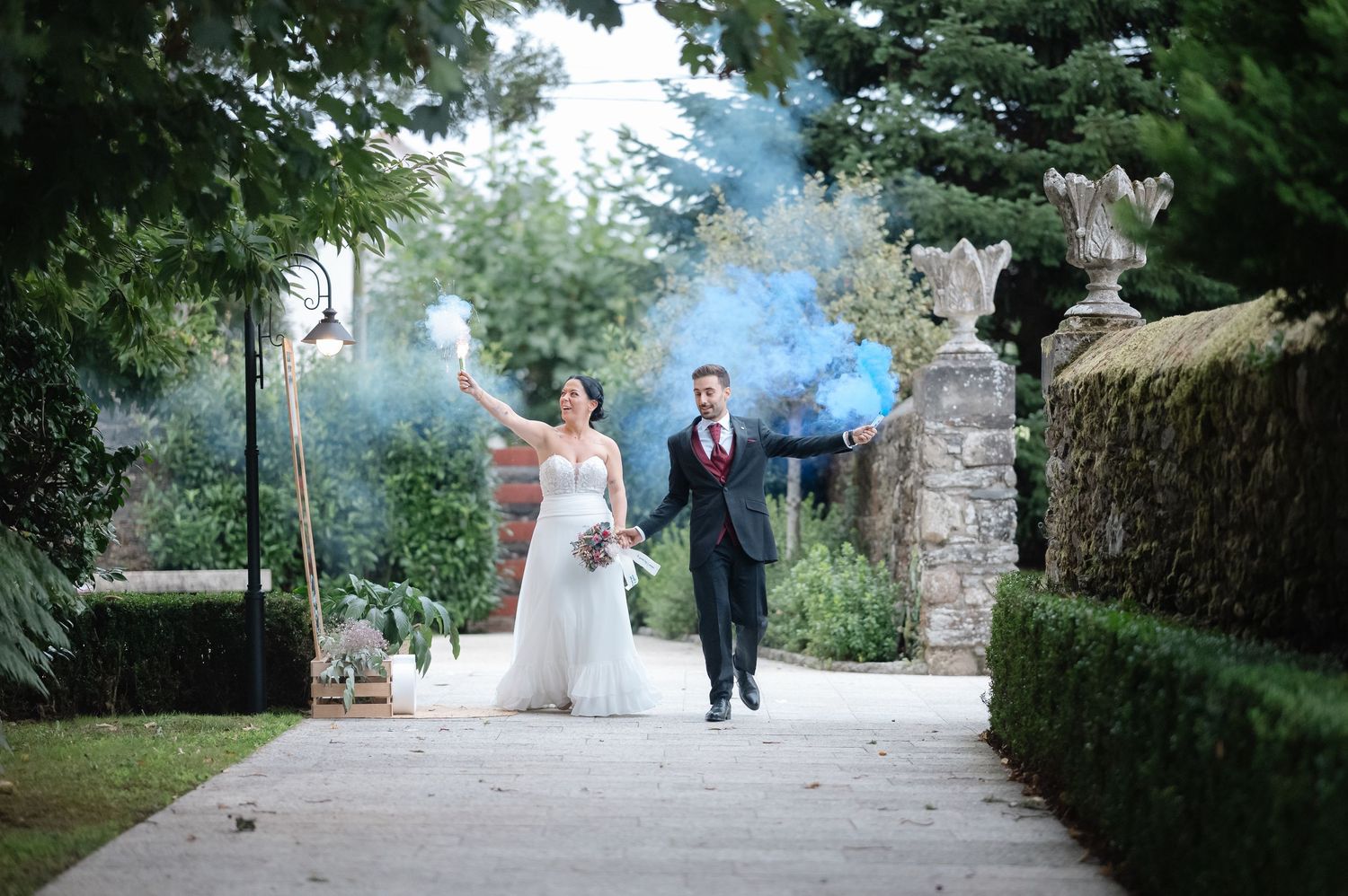 A couple walks down a scenic tree-lined path during a wedding celebration on a beautiful summer day.