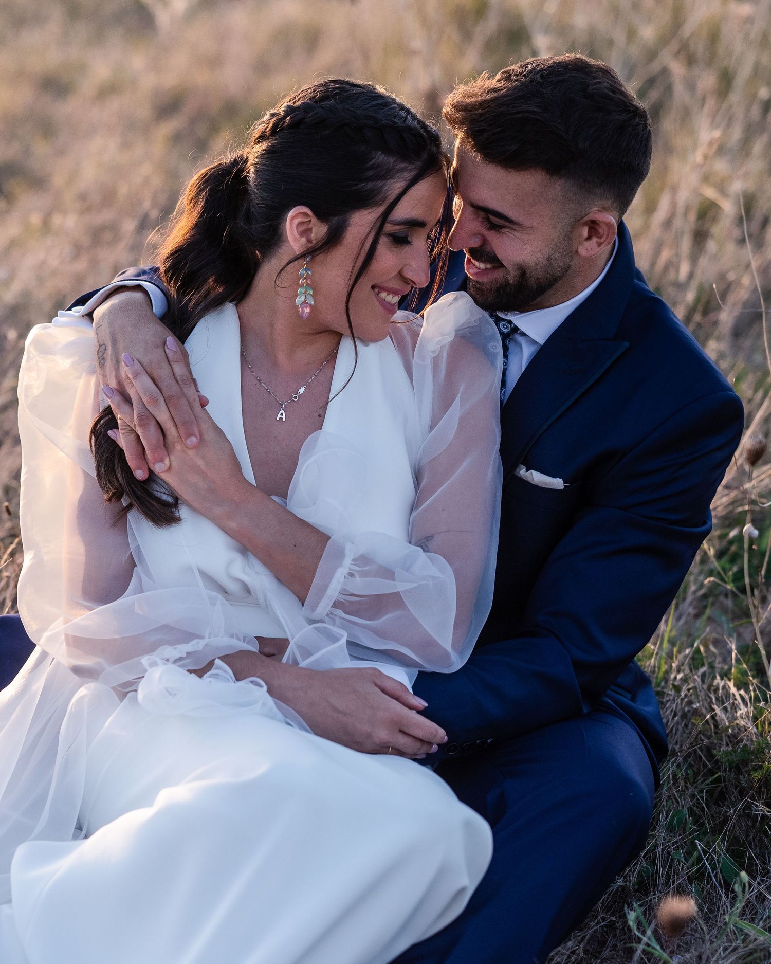 A couple in wedding attire share an intimate moment in a sunlit field during golden hour.