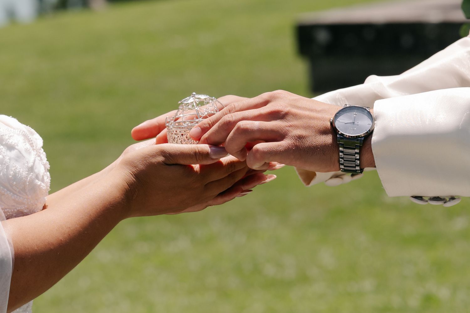 Hands exchanging wedding rings during an outdoor ceremony with green grass in the background.