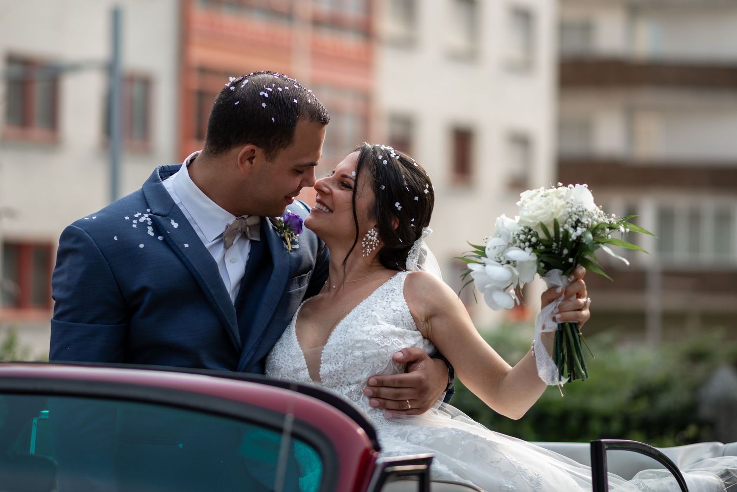 Newlyweds share a romantic kiss while holding a bouquet of flowers.