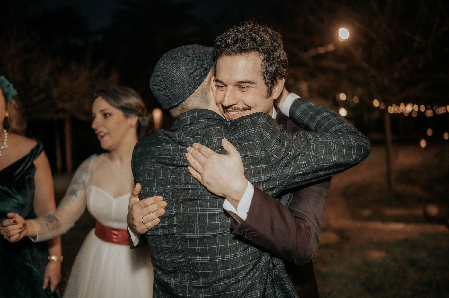 Two people share an emotional embrace during an outdoor evening wedding celebration.