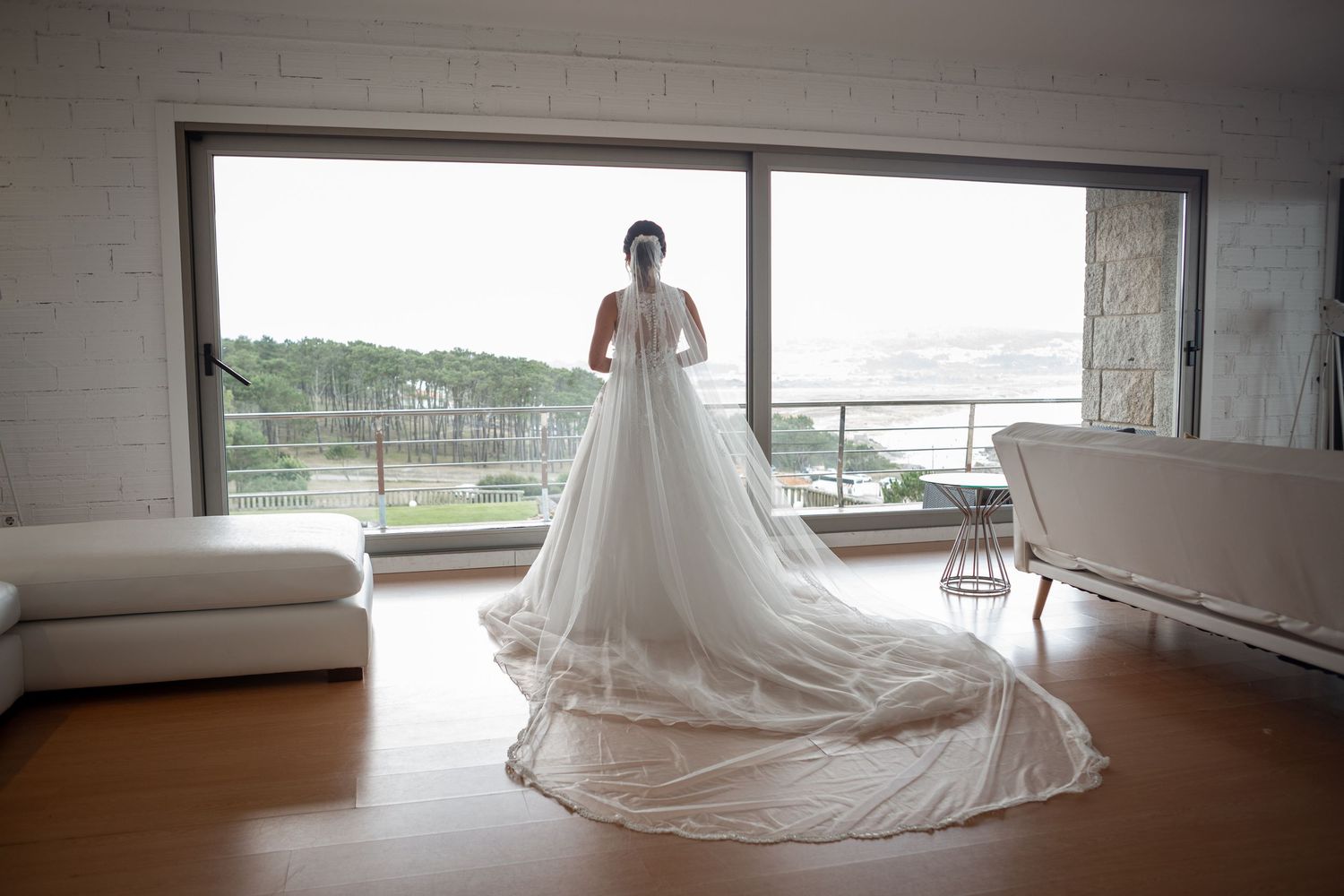 Panoramic view of a wedding dress with a long train in a modern room with large windows.