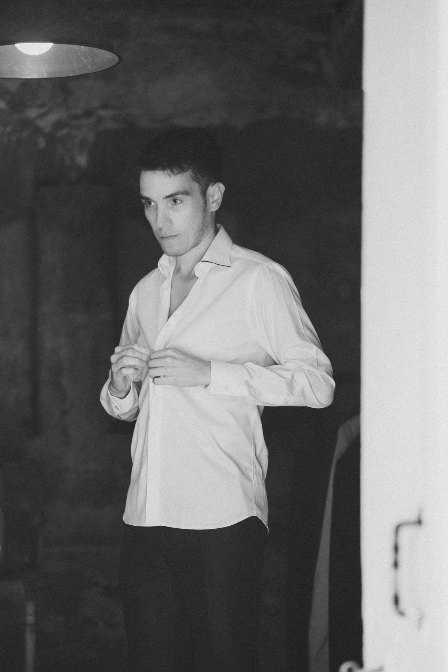Artistic black and white portrait shot of someone in a white shirt against a dark background.