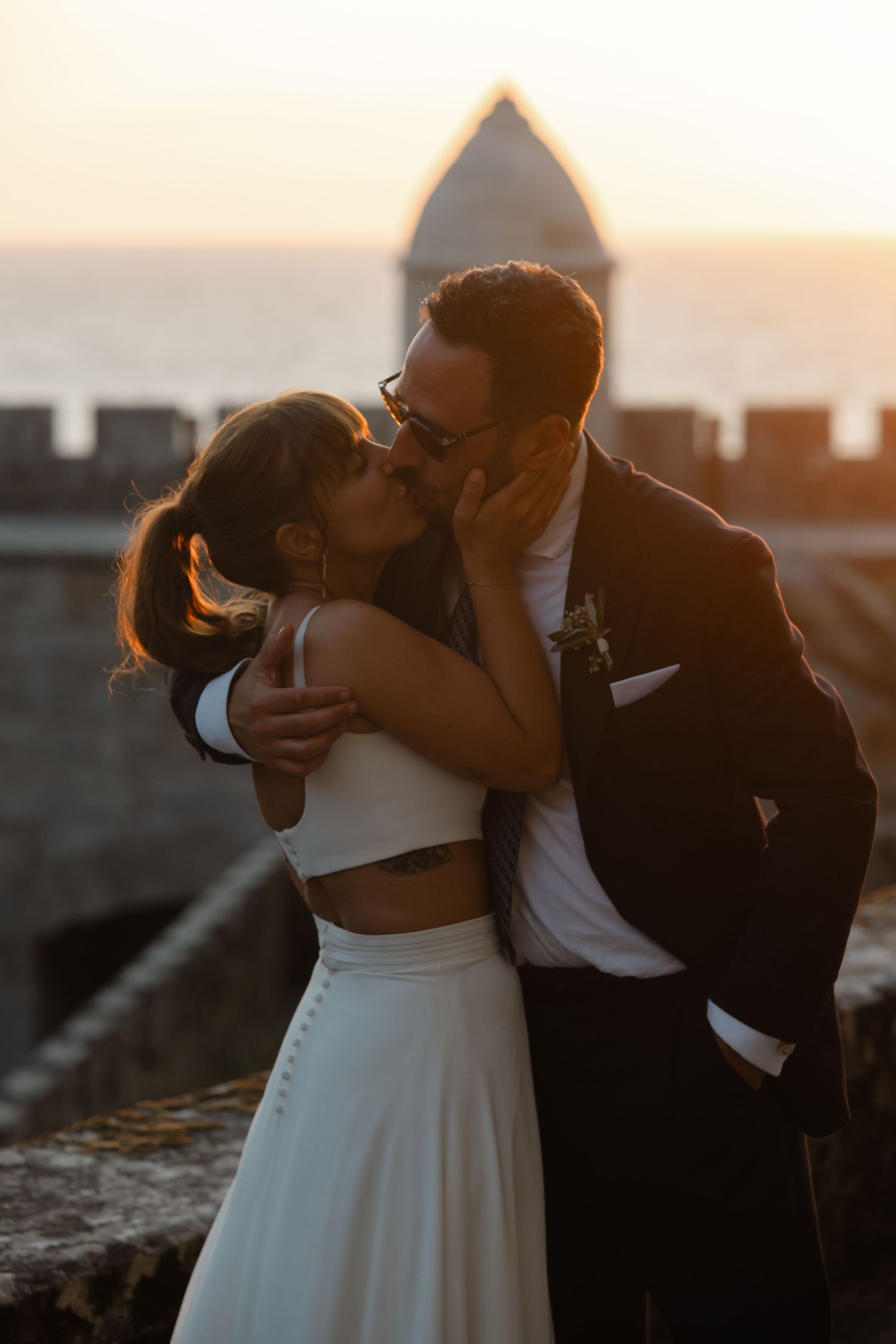 Silhouetted couple embracing during sunset with castle-like walls visible in the background.