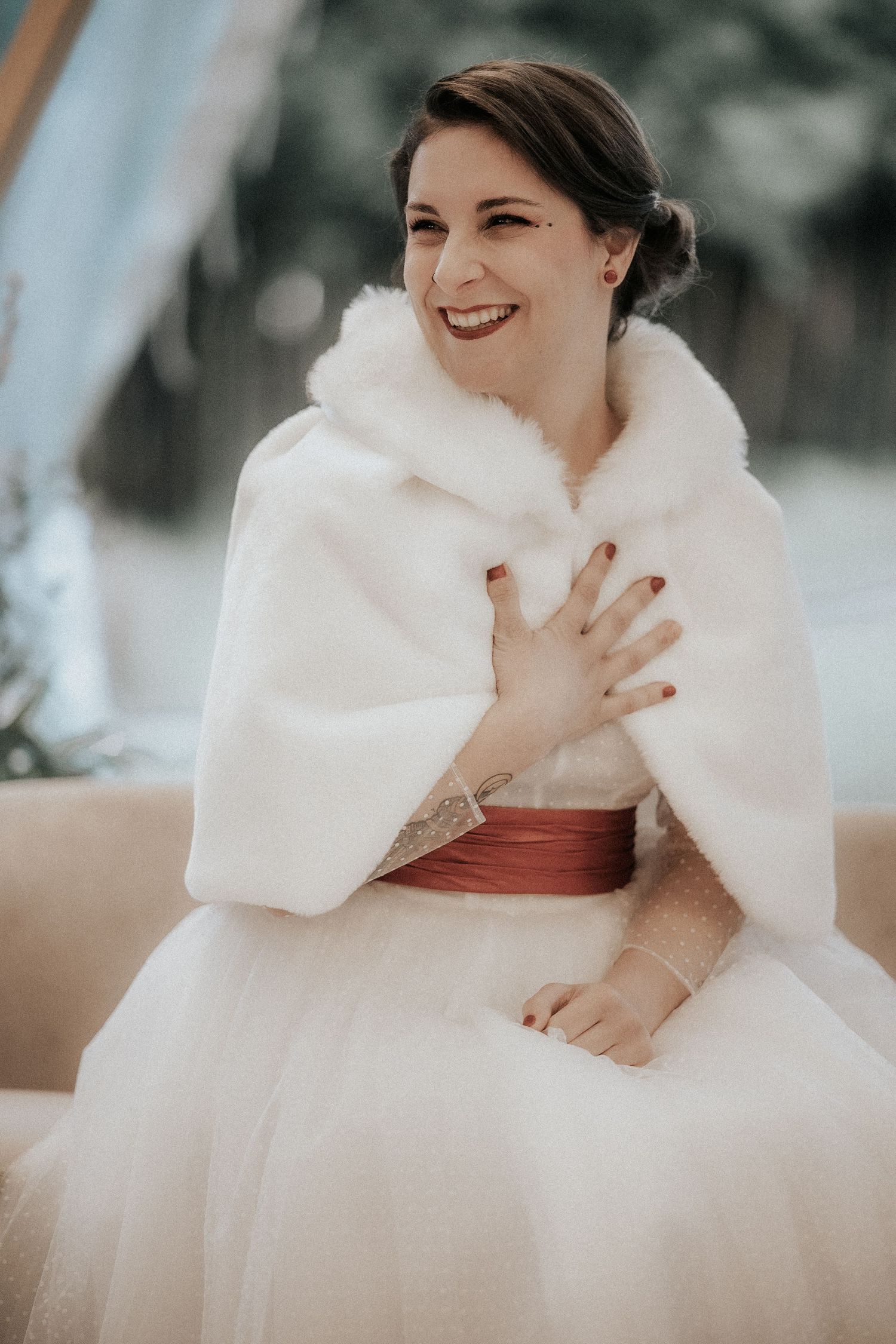 Bride wearing a white fur wrap and ballgown smiles joyfully during her winter wedding.