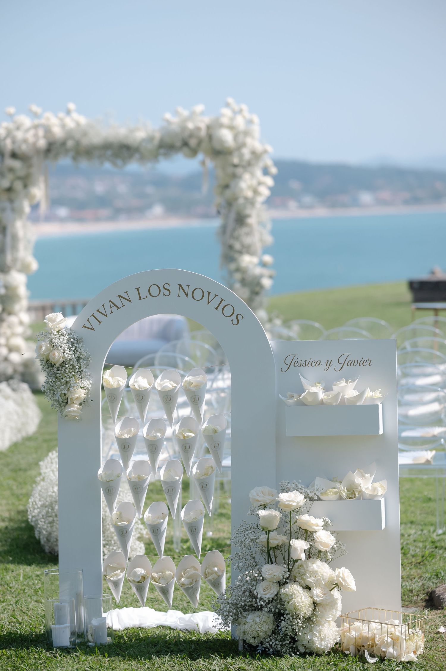 White wedding ceremony chairs with floral decorations arranged on a grassy oceanfront setting create an elegant outdoor venue.