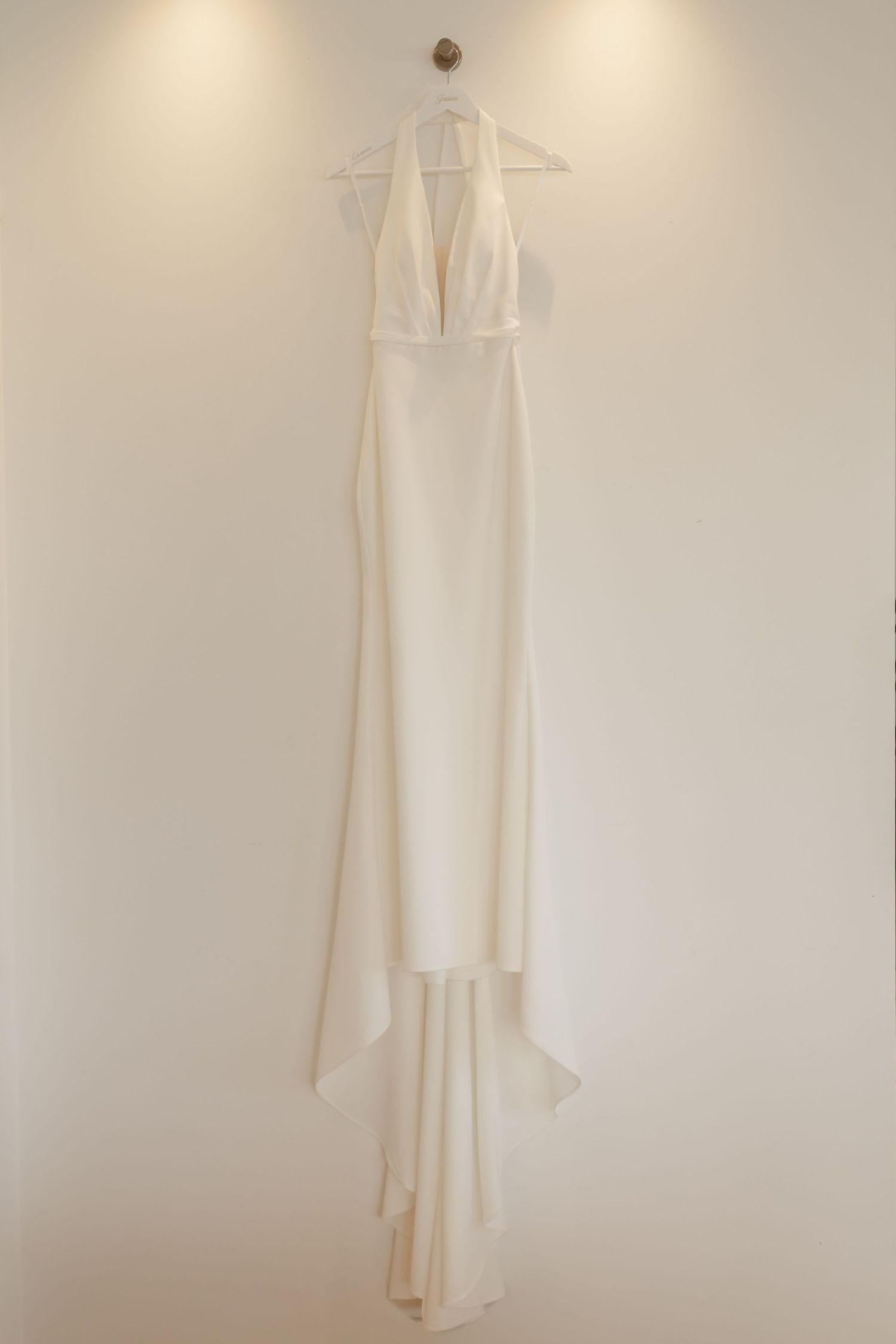 Minimalist white wedding dress hanging on display against a neutral wall.