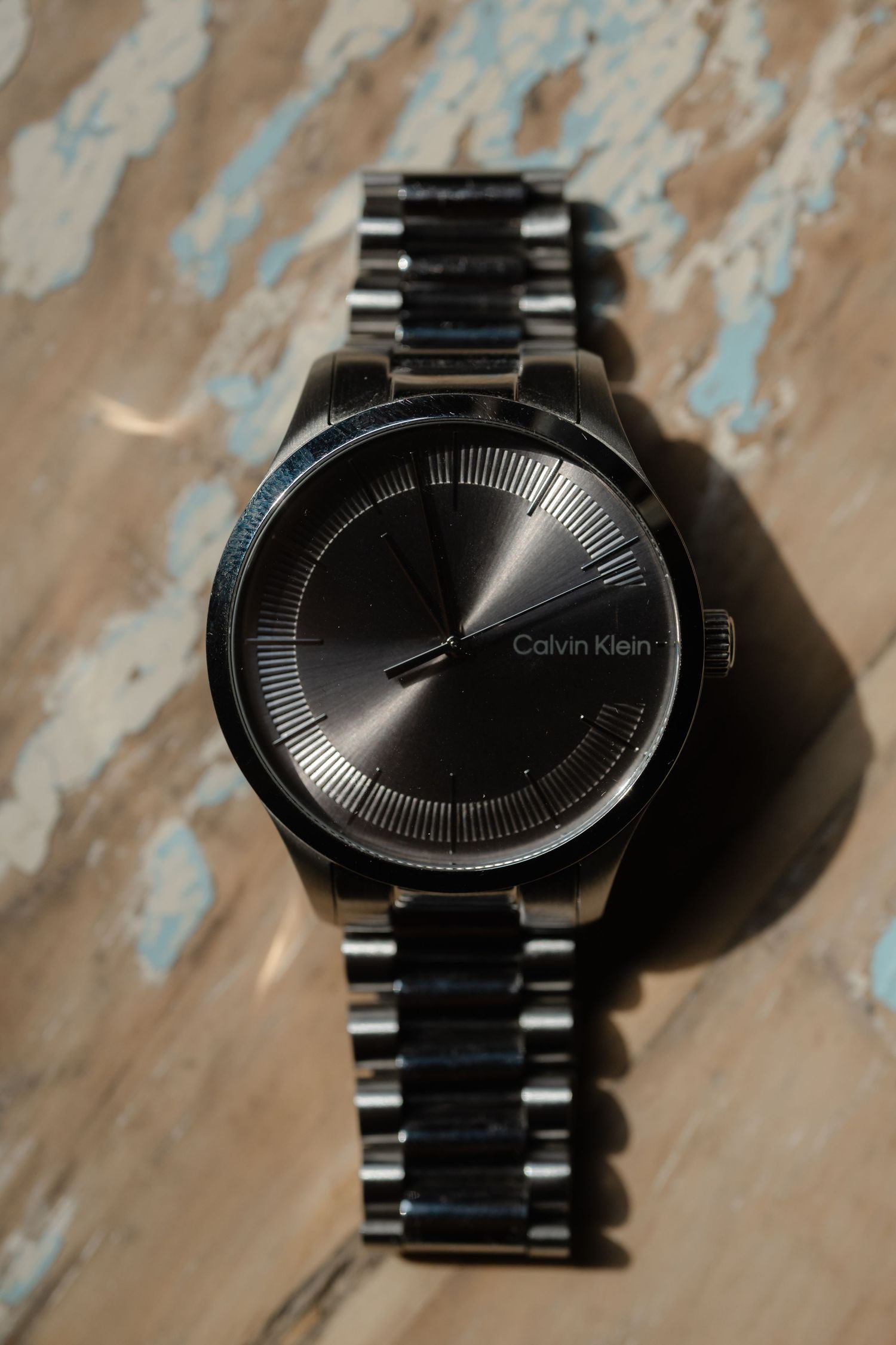 A sleek black Calvin Klein watch with minimalist design displayed on a distressed wooden surface.