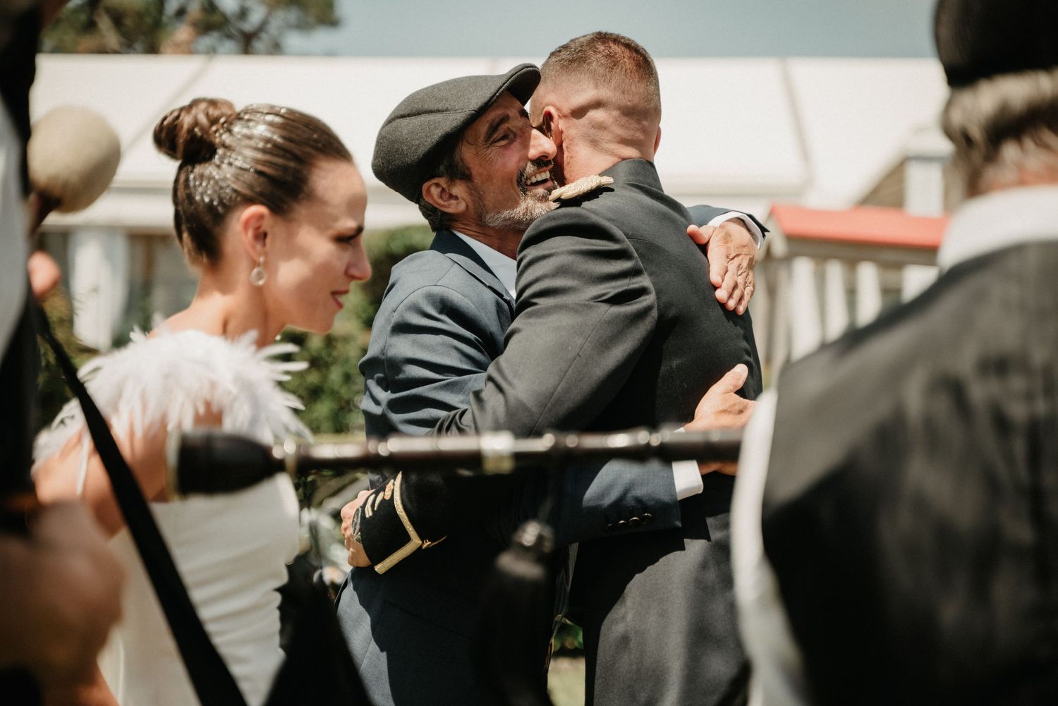 People share an emotional embrace at an outdoor gathering while others look on during a formal event.
