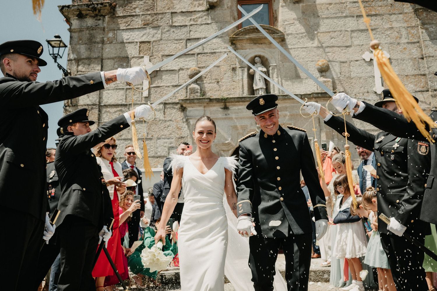 Newlyweds walk through military sword arch ceremony while guests celebrate with confetti.