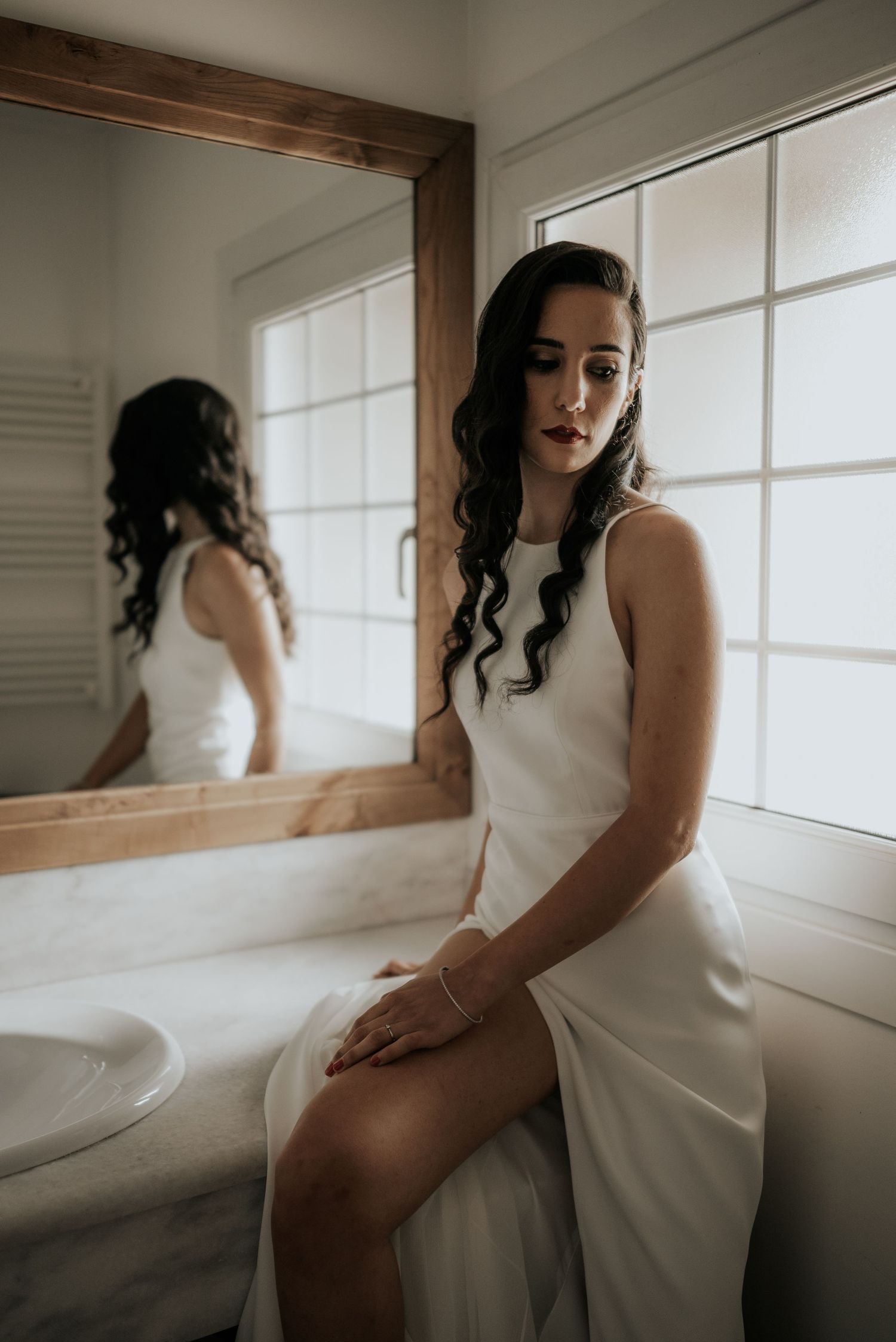 Artistic boudoir photo series showing a figure in a white dress seated by a window in moody natural light.