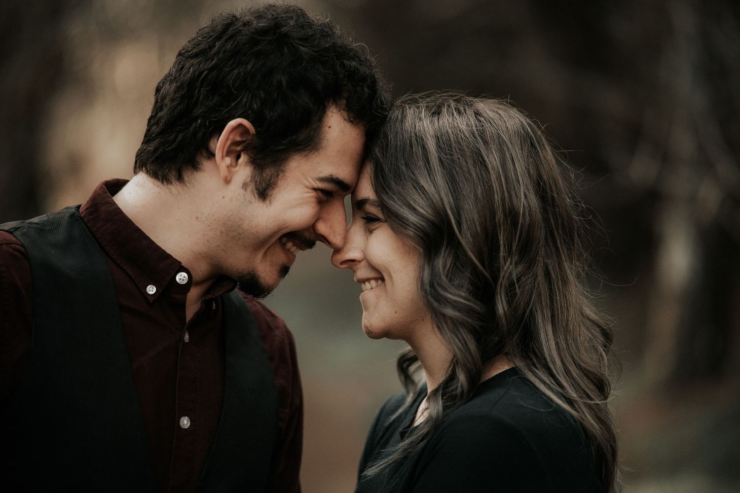 A couple shares an intimate moment in a moody forest setting with warm lighting.