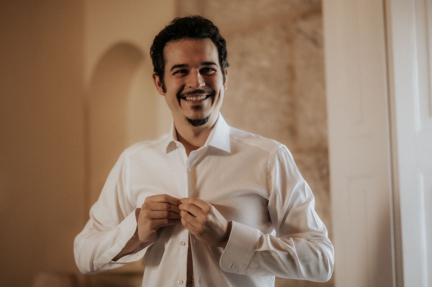 Someone in a white dress shirt smiles while holding a coffee cup in an elegant indoor setting.