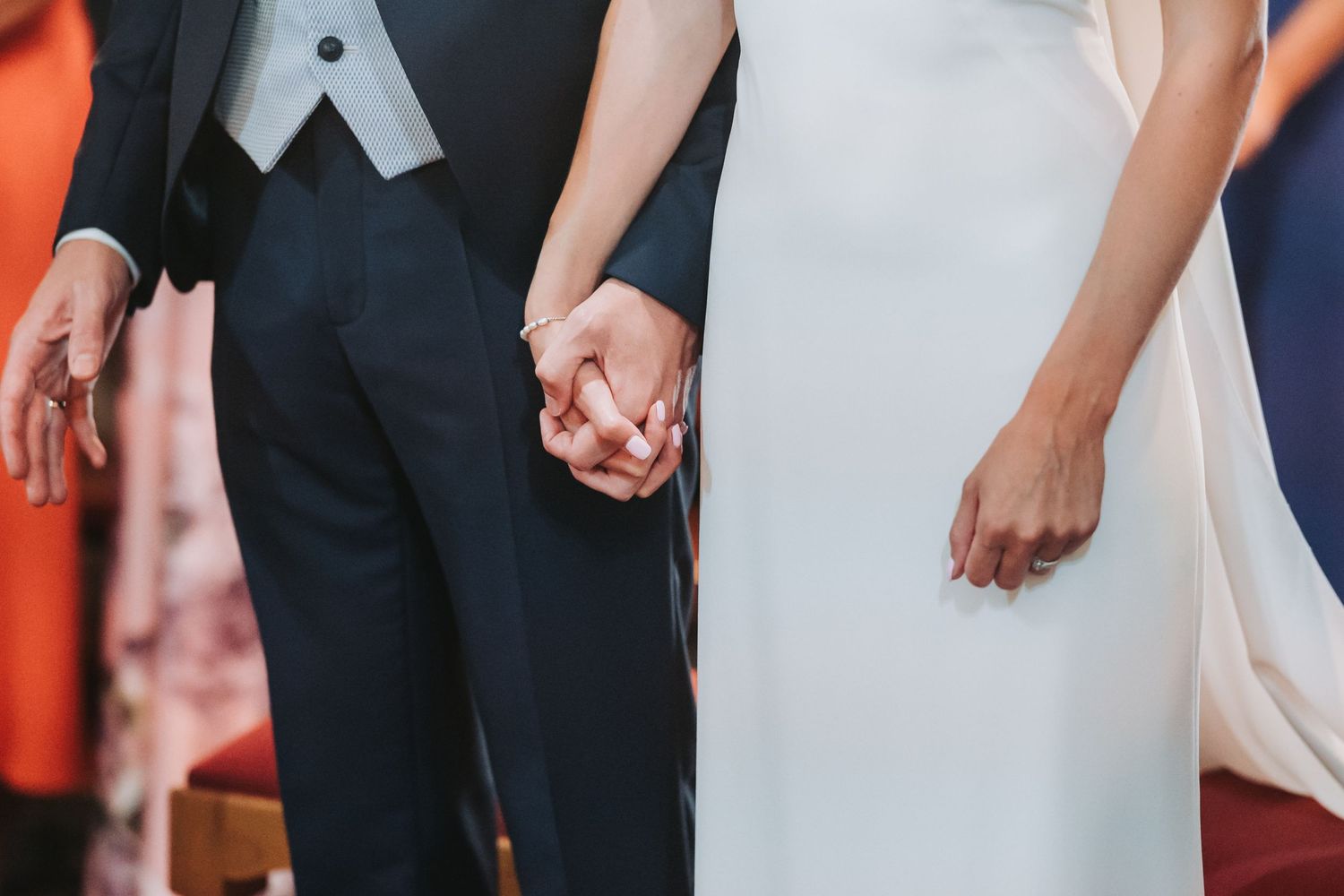 Close-up view of a couple holding hands at a wedding ceremony, with bride in white dress and groom in dark suit.