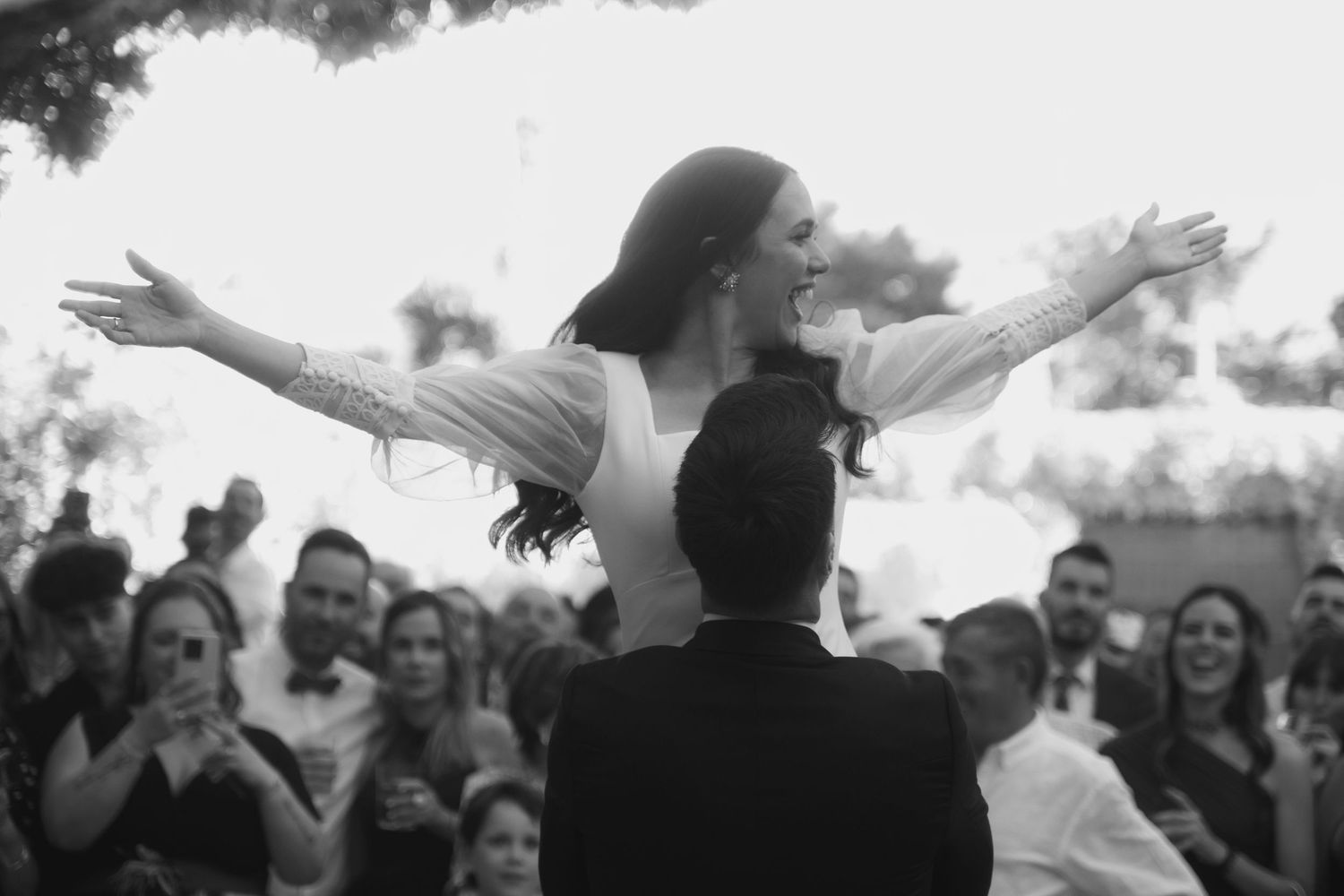 Black and white photo showing joyful wedding guests dancing and celebrating at a reception.