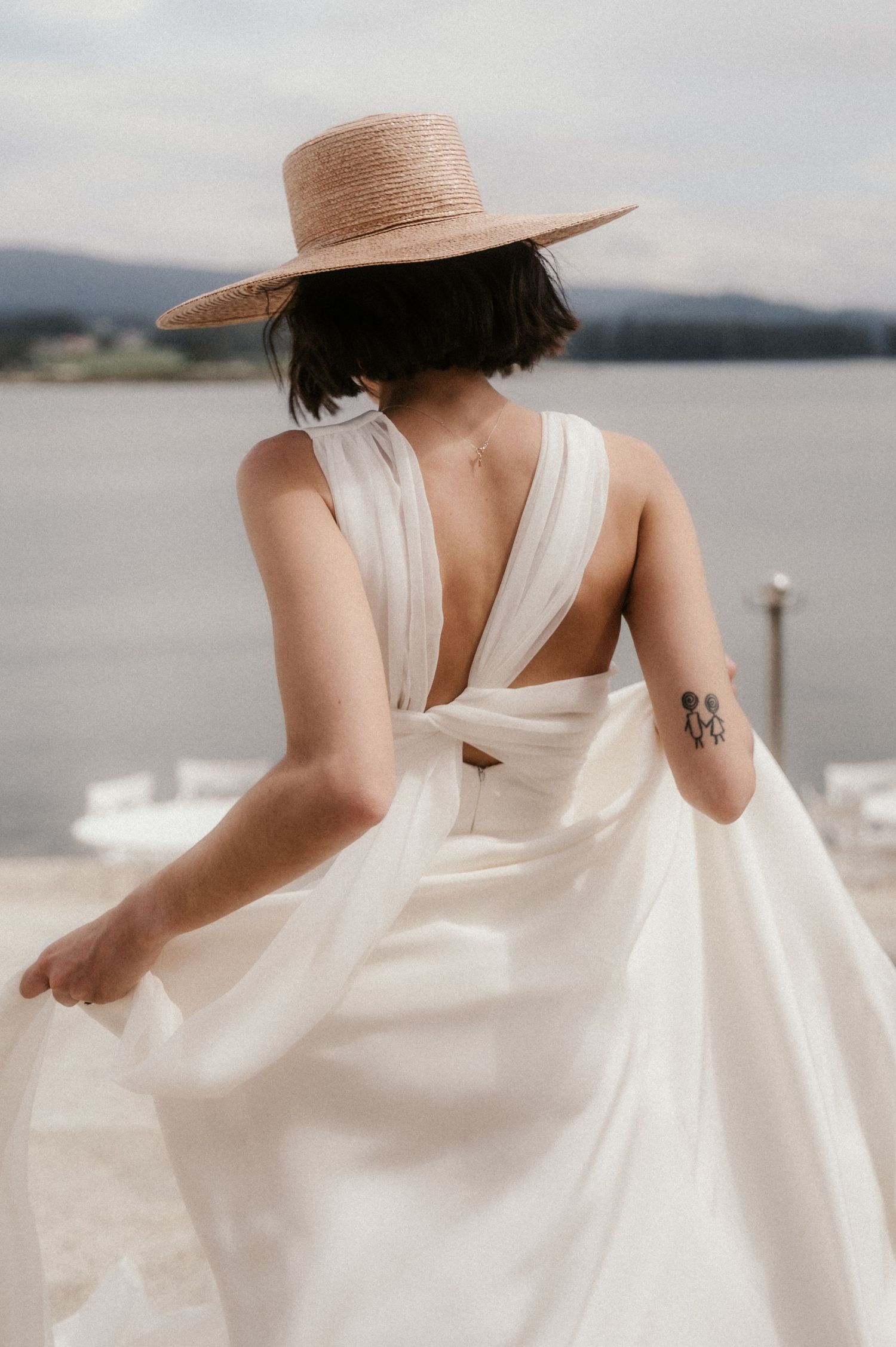 Ethereal white dress flowing in the breeze against a coastal backdrop with a straw hat and delicate details.