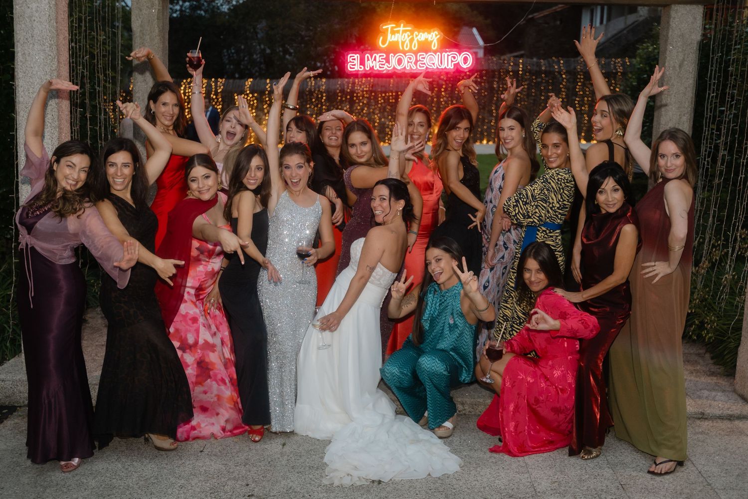 Wedding reception crowd celebrates under a red neon sign during an evening party.
