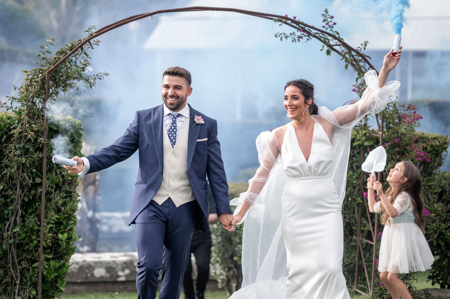 Wedding party celebrates joyfully outdoors with raised arms against a scenic coastal backdrop.