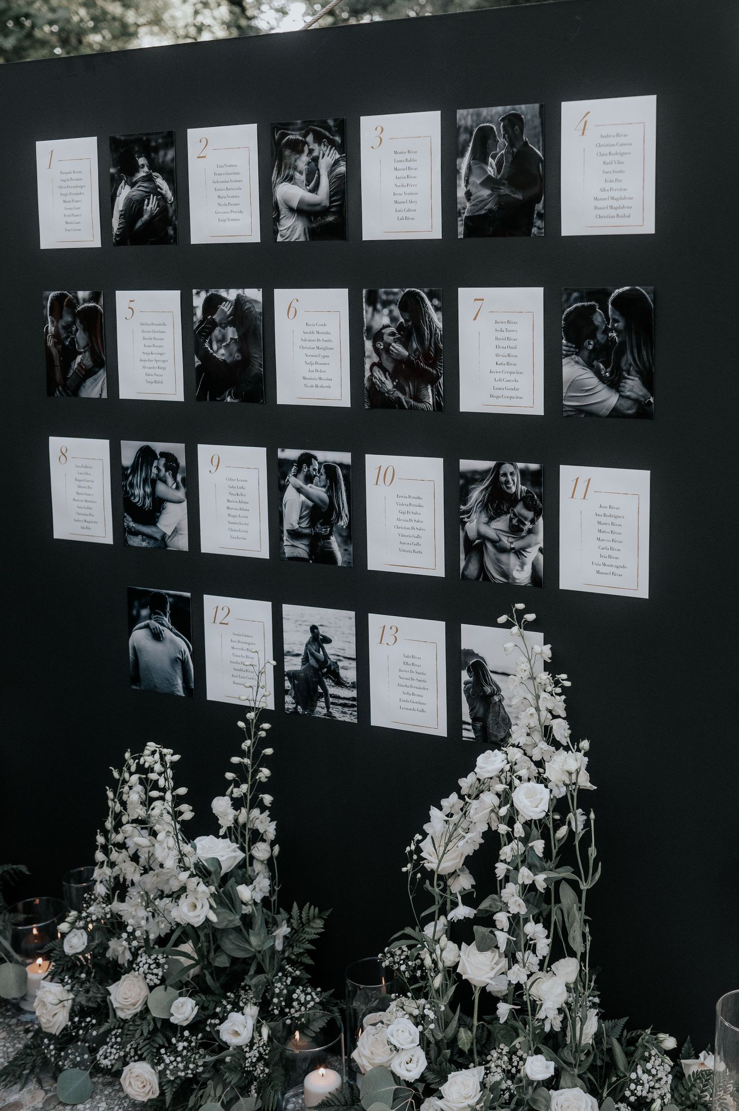 Black and white wedding photo display wall adorned with elegant floral arrangements and white roses at the base.