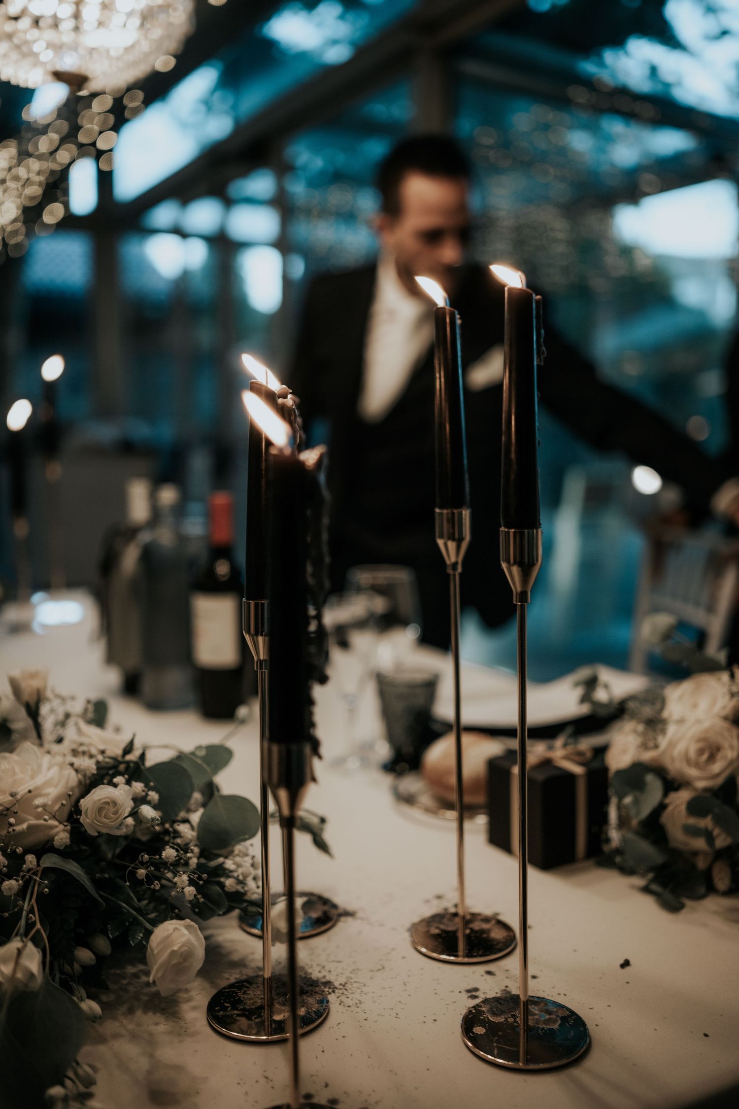 Elegant black candlesticks and floral arrangements create a moody wedding reception tablescape with dramatic lighting.