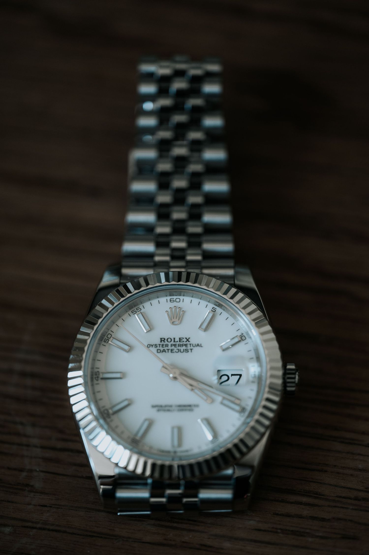 Close-up shots of a silver Rolex Datejust watch with fluted bezel and jubilee bracelet on a dark wooden surface.