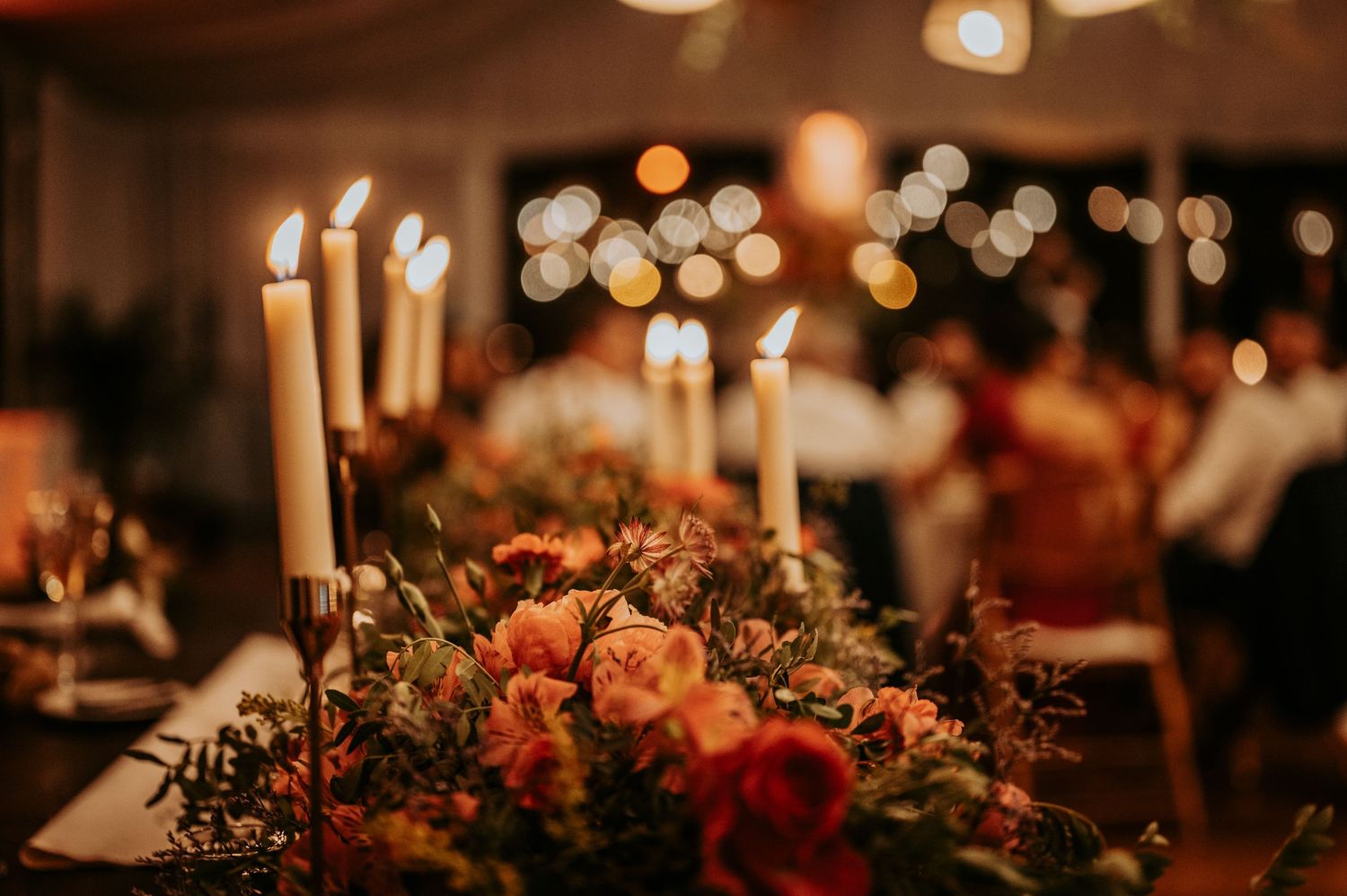 Romantic candlelit wedding table decorated with autumn-colored floral arrangements and taper candles.