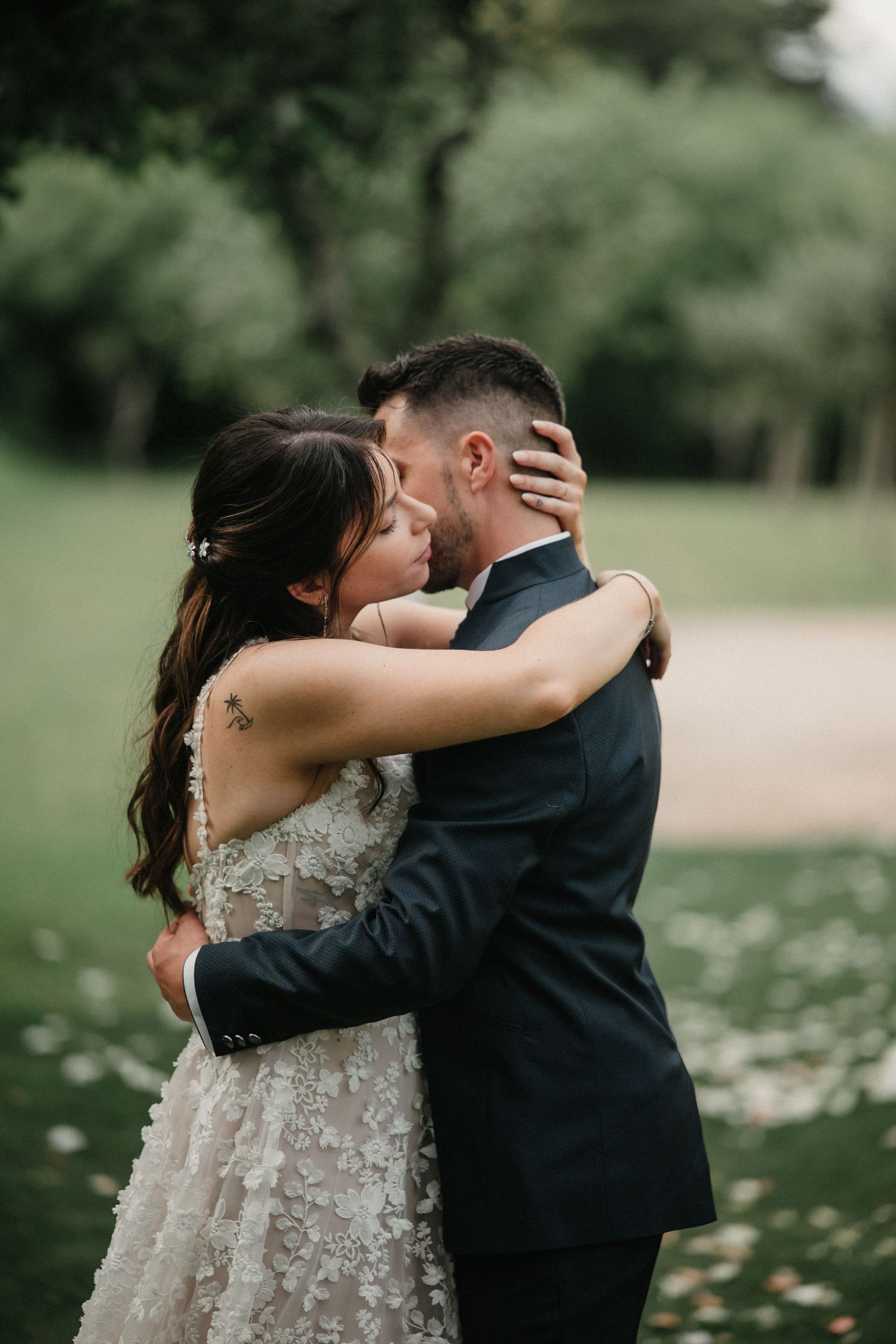 A couple shares an intimate moment outdoors in a garden setting with scattered white petals on the ground.